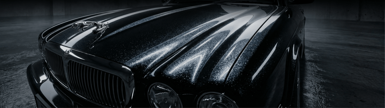 Close-up of the front hood and grille of a shiny black luxury car, with dramatic reflections of light highlighting its curves and metallic finish in a dimly lit garage.