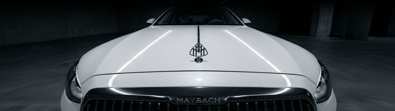 Front view of a white Mercedes-Maybach car in a dimly lit parking garage, highlighting the Maybach emblem on the hood and the grille.