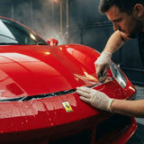 A man wearing gloves applies Transparent Glossy SelfRepair Nano-Coated PPF to the hood of a shiny red Ferrari in a workshop, ensuring invisible nano-coated protection for the car’s pristine finish. The Ferrari logo is clearly visible on the front.