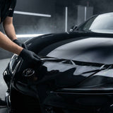 In a well-lit garage, a person in black gloves applies Transparent Glossy SelfRepair Nano-Coated PPF to the hood of a shiny black Toyota, providing invisible protection.