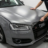 A person is applying Transparent Matte SelfRepair Nano-Coated PPF to the hood of a gray Audi S Series, partially covering the front headlight and grille.