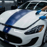 Wearing blue gloves, a person applies Transparent Matte SelfRepair Nano-Coated PPF to the hood of a white sports car with blue racing stripes in a garage.