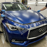 Two people in blue gloves apply Transparent Matte Sparkle SelfRepair Nano-Coated PPF to the hood of a blue Infiniti sedan inside a garage.