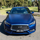 A blue Infiniti sedan with Transparent Matte Sparkle SelfRepair Nano-Coated PPF is parked on pavement by a park with green grass, trees, and sunlight in the background, viewed from the front.
