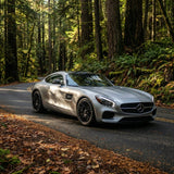A silver Mercedes-Benz sports car with Satin Aluminum Mercury SelfRepair Nano-Coated PPF is parked on a winding road in a lush green forest, showcasing advanced body protection in daylight.