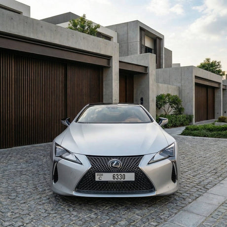 A silver Lexus wrapped in Satin Ceramic White SelfRepair Nano-Coated PPF is parked on a cobblestone driveway, framed by modern concrete homes with wooden garage doors and landscaped greenery.