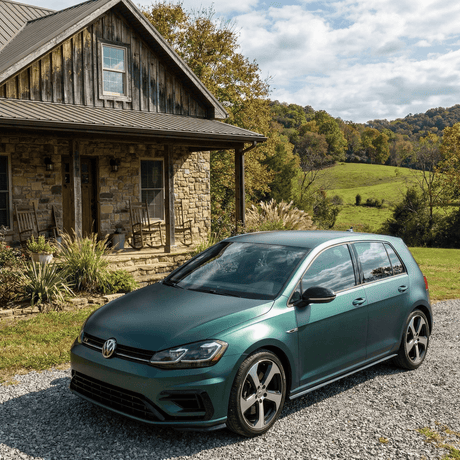 A Volkswagen hatchback wrapped in Satin Venom Green SelfRepair Nano-Coated PPF is parked on a gravel driveway before a rustic stone house, surrounded by lush hills and trees under a partly cloudy sky.