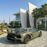A Lamborghini with Satin Khaki Green SelfRepair Nano-Coated PPF is parked on a stone driveway by a modern white house, with palm trees and city skyscrapers like the Burj Khalifa visible in the background.