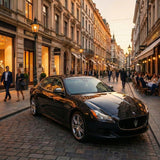 A sleek black Maserati protected with Diamond Havana Black Glossy SelfRepair Nano-Coated PPF is parked on a cobblestone street lined with elegant shops like Gucci and Armani, while people stroll and dine outdoors in the warm evening light.