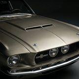 Close-up of the front end of a classic gold Ford Mustang Shelby GT500, showing the hood scoop, headlights, and Shelby badging against a dark background.