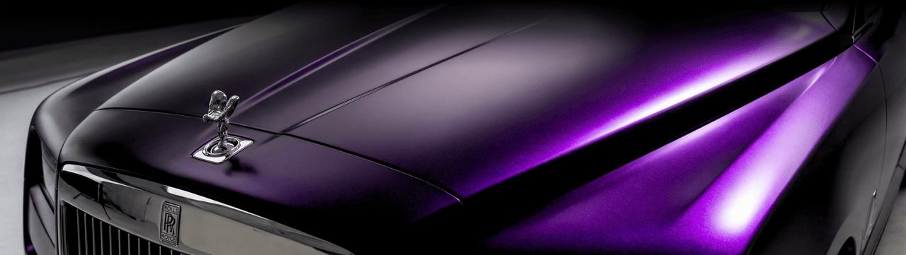 Close-up of a luxury car hood in a glossy metallic purple finish, featuring the iconic Rolls-Royce Spirit of Ecstasy hood ornament and part of the chrome front grille.
