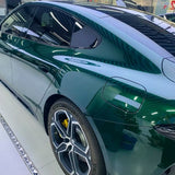 A shiny green electric car in Agate Green Liquid Metallic Glossy SelfRepair Nano-Coated PPF is seen from the side, displaying its rear door, sleek lines, dark tinted windows, and alloy wheels with yellow brake calipers under bright indoor lights.