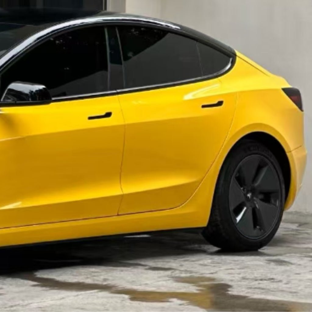 A bright yellow sedan with tinted windows and black wheels, protected by Amber Yellow Glossy SelfRepair Nano-Coated PPF, is parked on a concrete surface near a light-colored wall. Only the rear half of the car is visible.