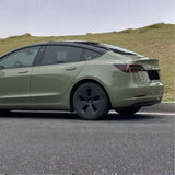 A Tesla Model 3 wrapped in Army Green Glossy SelfRepair Nano-Coated Nexthor™ PPF is parked roadside, with grassy hills and an overcast sky in the background.