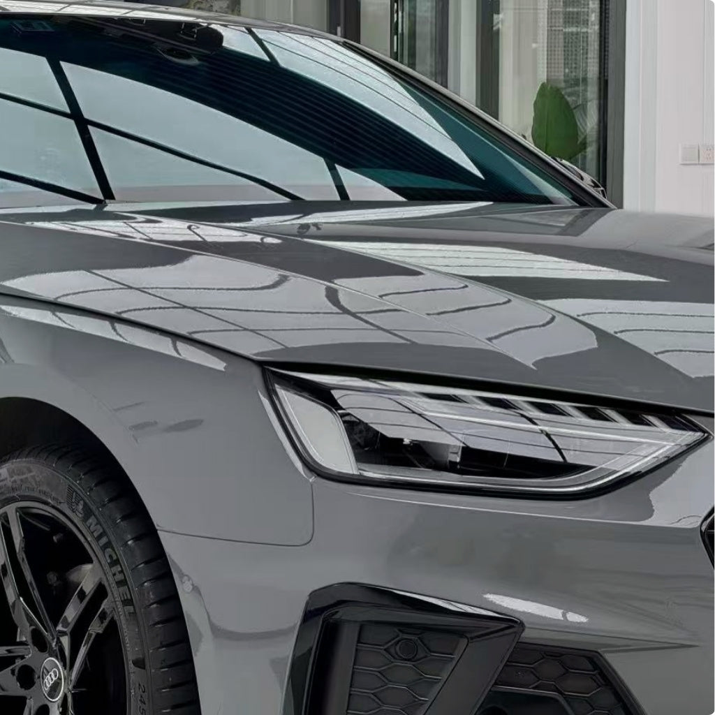 Close-up of the front left side of a modern car with Audi Nardo Gray Glossy SelfRepair Nano-Coated PPF, featuring a sleek headlight, black alloy wheel, and glossy reflections on bodywork shielded by this premium protective film.