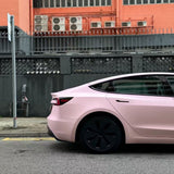 A Baby Pink SelfRepair Nano-Coated PPF car is parked by a black fence, near a peach building with several AC units, highlighting its ochrana proti škrabancom for lasting beauty.