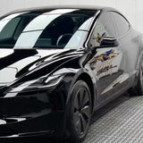 A black Tesla Model S with Black Glossy SelfRepair Nano-Coated PPF is parked indoors on a patterned floor, its paint reflecting the lights and surroundings while the PPF provides extra protection.