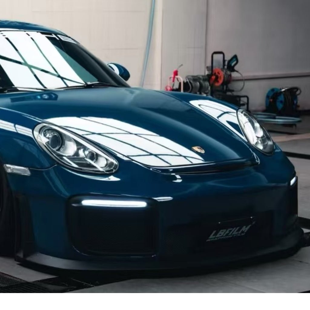 A shiny blue Porsche, shielded by Deep Blue Glossy SelfRepair Nano-Coated PPF, is parked indoors under bright lights with reflections on its hood and windshield. Automotive equipment appears in the background.