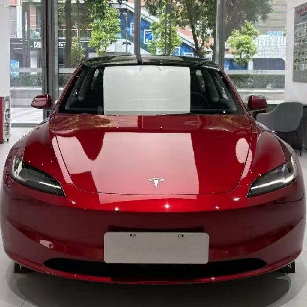 A red Tesla with a sleek design is showcased indoors by large windows, its finish enhanced by Deep Red Glossy SelfRepair Nano-Coated PPF, an ochranná fólia na auto reflecting trees and buildings outside.