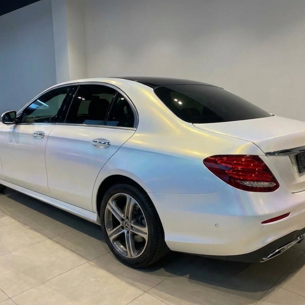 A white luxury sedan with tinted windows and alloy wheels is parked indoors, its rear side gleaming under bright lighting, protected by White Diamond Blue Glossy SelfRepair Nano-Coated PPF for a stunning, durable finish.