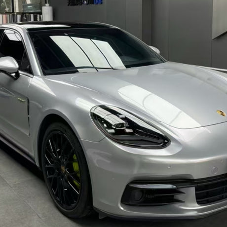 A silver Porsche sedan with black wheels is parked indoors in a modern garage, its finish protected by GT Silver Liquid Metallic Glossy SelfRepair Nano-Coated PPF for enhanced shine and durability.