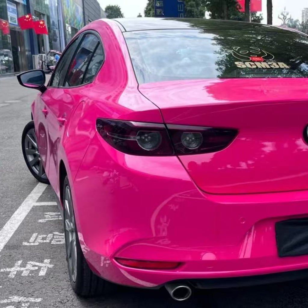 A bright pink sedan with Hot Crush Glossy SelfRepair Nano-Coated PPF for body protection is parked near buildings with Chinese flags. The rear view shows tinted windows, dark taillights, and a SENBA decal on the back windshield.