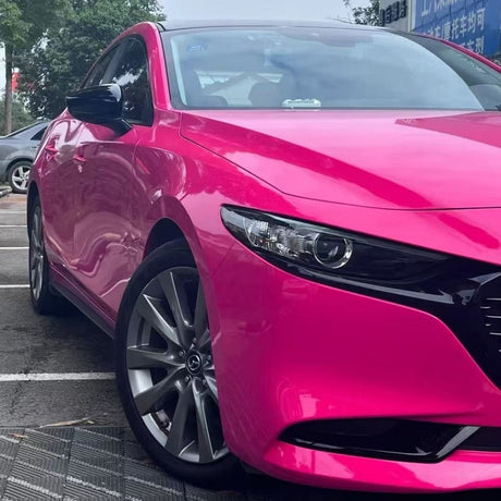 A bright pink sedan with Hot Crush Glossy SelfRepair Nano-Coated PPF is parked outdoors. Its front and side reflect trees and signs, showing off the shiny, protected paint finish.