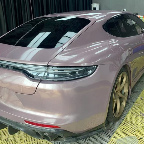 A Porsche sports car in metallic mauve, wrapped in Ice Berry Pink Liquid Metallic Glossy SelfRepair Nano-Coated PPF, sits indoors on a yellow-patterned floor. Gold wheels and dark-tinted windows complete the striking appearance.