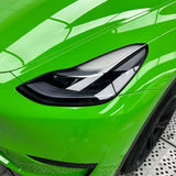 Close-up of a Lizard Green Glossy SelfRepair Nano-Coated PPF car's headlight, featuring sharp lines and a reflective surface, with part of the wheel and patterned floor visible.