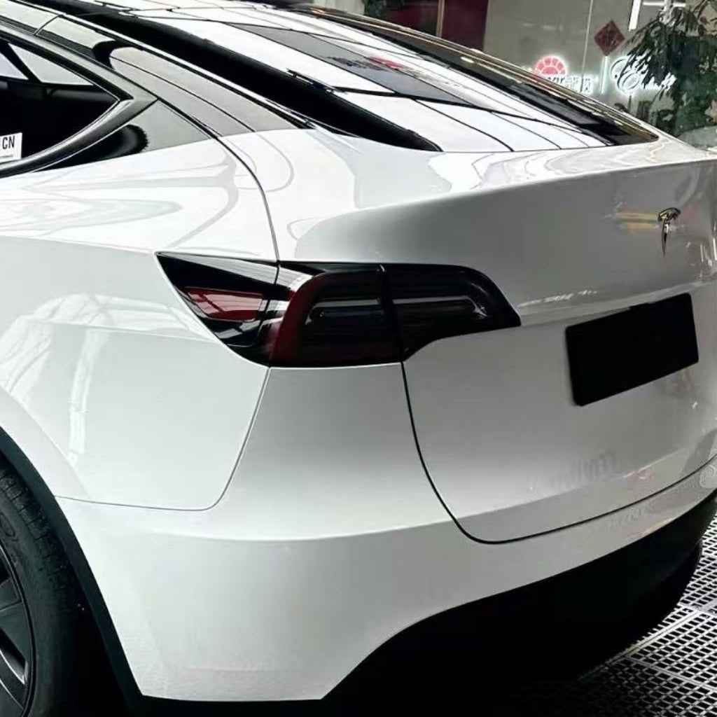 A close-up of the rear of a white Tesla, showcasing its sleek taillights and aerodynamic lines, protected by Metallic White Glossy SelfRepair Nano-Coated PPF in a modern showroom.