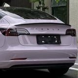 Rear view of a white Tesla parked on the street, with the Tesla logo above the license plate. Tail lights and rear window are visible, while Misty Gray Purple Glossy SelfRepair Nano-Coated PPF adds subtle color protection to the paint.
