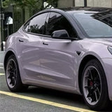 A sleek, silver electric car with Misty Gray Purple Glossy SelfRepair Nano-Coated PPF is parked by the street, its tinted windows reflecting buildings and trees nearby.