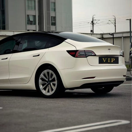 A white Tesla Model 3 with a VIP plate, protected by Pepper White Glossy SelfRepair Nano-Coated PPF, is parked in a lot with a modern building and fencing visible in the background.