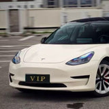 A white Tesla with a green VIP license plate is parked outdoors, featuring a Pepper White Glossy SelfRepair Nano-Coated PPF for extra shine; buildings can be seen in the background.