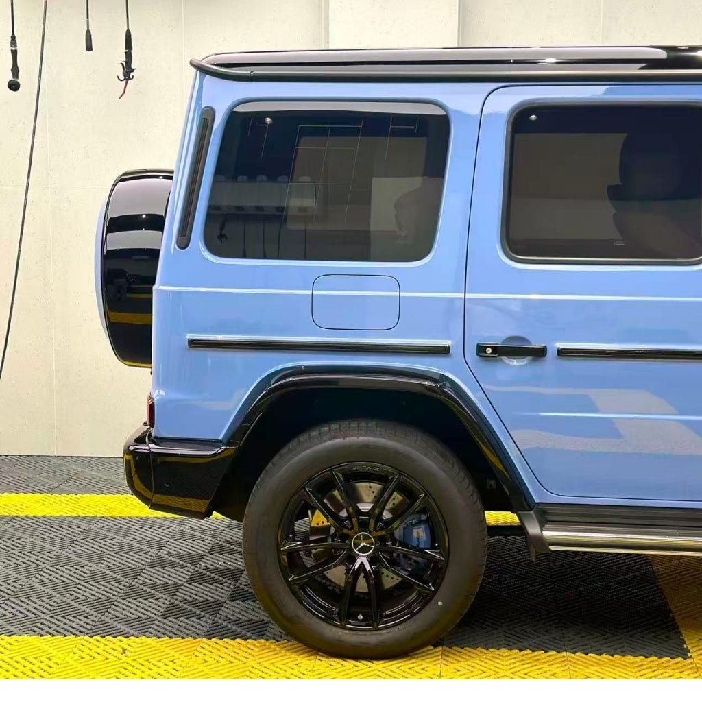 A partial side view of a light blue Mercedes-Benz SUV with tinted windows and black wheels showcases its rear protected by Porcelain Blue Glossy SelfRepair Nano-Coated PPF, parked indoors on a yellow and black mat.