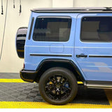 A partial side view of a light blue Mercedes-Benz SUV with tinted windows and black wheels showcases its rear protected by Porcelain Blue Glossy SelfRepair Nano-Coated PPF, parked indoors on a yellow and black mat.