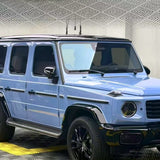 A Mercedes-Benz G-Class SUV in Porcelain Blue Glossy SelfRepair Nano-Coated PPF with black trim and wheels is parked indoors on a patterned floor, its paint protected by advanced self-healing nano-coating and set against a textured wall.