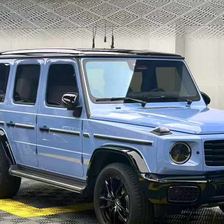 A Mercedes-Benz G-Class SUV in Porcelain Blue Glossy SelfRepair Nano-Coated PPF with black trim and wheels is parked indoors on a patterned floor, its paint protected by advanced self-healing nano-coating and set against a textured wall.