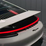 Close-up of the rear of a white Porsche 911 with a prominent spoiler, red LED tail light strip, and Porsche lettering—highlighting paint protection by Porsche Gray Glossy SelfRepair Nano-Coated PPF against a sleek gray background.