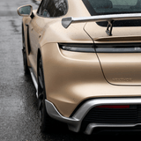 Rear view of a beige sports car featuring Liquid Metallic Aluminium Carbon Fiber Self-Healing Nano-Coated PPF, with water droplets highlighting its sleek taillight, spoiler, rear tire, and aerodynamic details on a wet road.