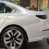 Close-up of a white BMW sedan's rear with Arctic White Sparkle Glossy SelfRepair Nano-Coated PPF ochrana karosérie; intricate rims and taillight pop against the showroom background.