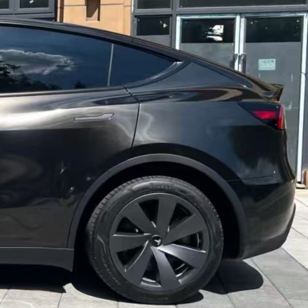 A close-up side view of the rear half of a black Tesla Model Y, parked outside a building, showcasing tinted windows and reflections on the sleek surface of Diamond Black Gold Glossy SelfRepair Nano-Coated Nexthor™ PPF.