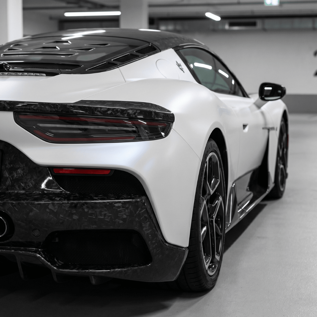 A sleek white sports car with a black roof and carbon fiber accents features a Forged Carbon Graphite Self-Healing Nano-Coated PPF, parked indoors and viewed from a rear side angle.