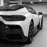 A sleek white sports car with a black roof and carbon fiber accents features a Forged Carbon Graphite Self-Healing Nano-Coated PPF, parked indoors and viewed from a rear side angle.