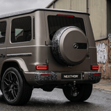 A matte gray Mercedes-Benz SUV is parked on a wet street near an industrial building, featuring a bold Forged Carbon Graphite Self-Healing Nano-Coated PPF finish and a NEXTHOR plate for a striking rear view.