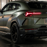 A luxury matte green SUV featuring Matte Carbon Fiber SelfRepair Nano-Coated PPF is parked on a city street at night, highlighted by sharp lines, large black wheels, and striking red LED tail lights under the streetlights.