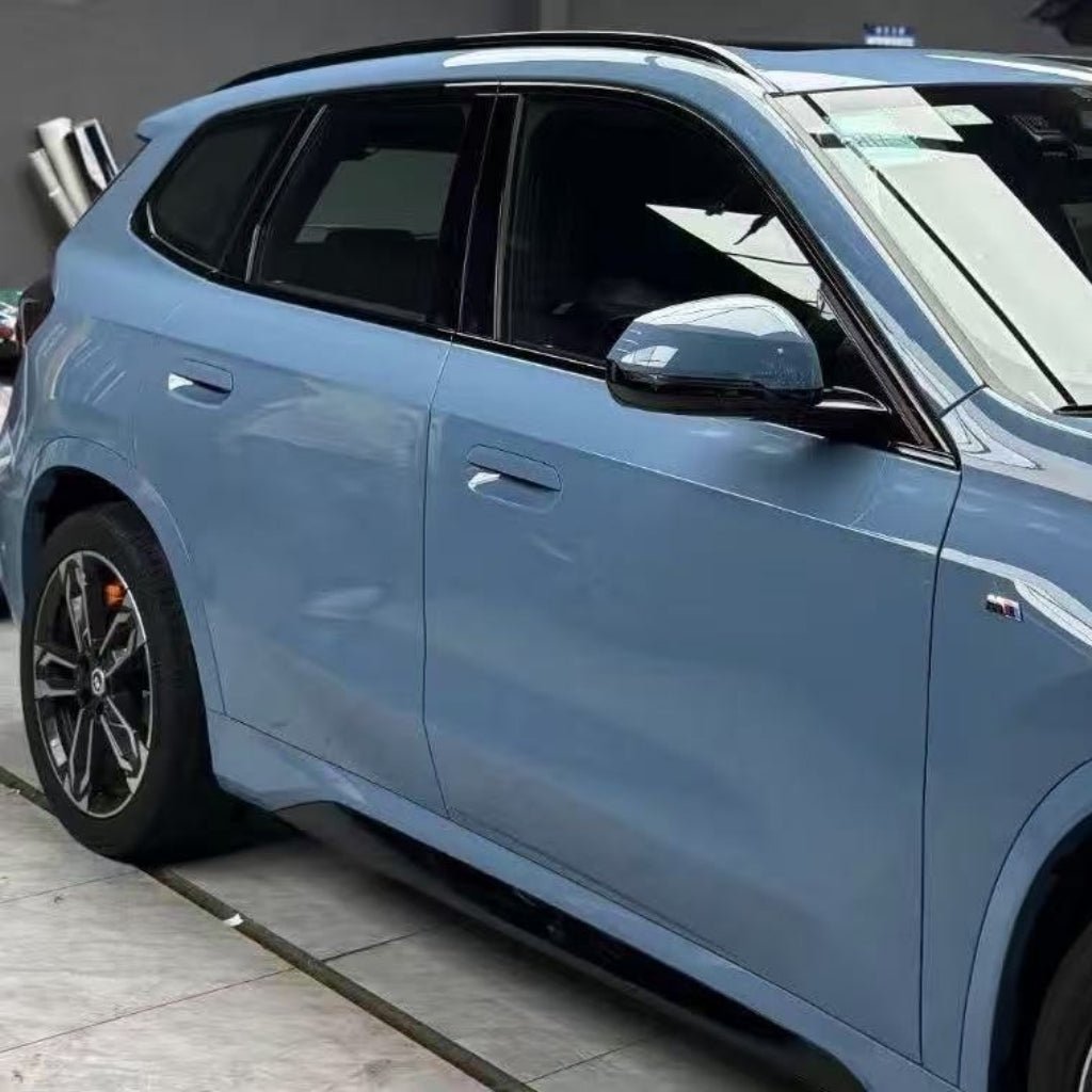 A light blue SUV is parked indoors, side view visible with tinted windows, black trim, sporty alloy wheels, and Blue Lagoon Glossy SelfRepair Nano-Coated PPF for vynikajúca ochrana laku vozidla.