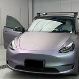 A matte lavender Tesla Model 3 with Capri Gray Purple Matte SelfRepair Nano-Coated PPF has its driver-side door open inside. The car sports a roof rack and has a blacked-out front license plate.