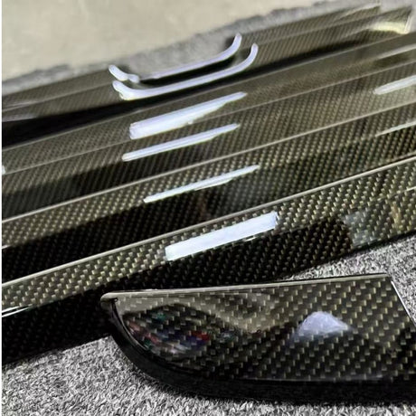 Close-up of several Carbon Fiber Carbon SelfRepair Nano-Coated PPF trim pieces featuring a black and grey weave pattern, displayed on a textured grey surface.