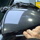 A person applies Carbon Fiber Carbon SelfRepair Nano-Coated PPF to a car’s side mirror, carefully smoothing the protective film over the surface with their hand.